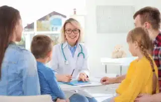 A doctor smiling with a happy family in the background