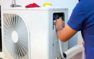 A professional HVAC technician inspects a clean, efficient heat pump system outside a modern home.
