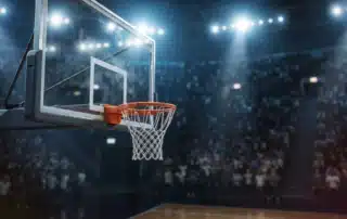 Glass basketball backboard and hoop in a brightly lit arena, showcasing backboard size and design for optimal home basketball court performance.