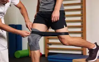 Sports medicine specialist assessing a patient’s knee during a rehabilitation exercise to identify pain, instability, or signs of a sports injury.
