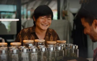 Smiling Asian budtender standing behind a counter with many jars of cannabis in Mystic CT